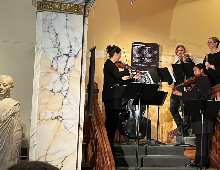 A group of musicians performing at Medelhavsmuseet, with a marble statue on the left and a sign in the background. Photo by Ingrid Stigsdotter.
