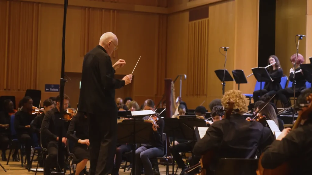 A conductor leads an orchestra during a performance at the Tower Hamlets Arts & Music Education Service (THAMES) 2024 festival.