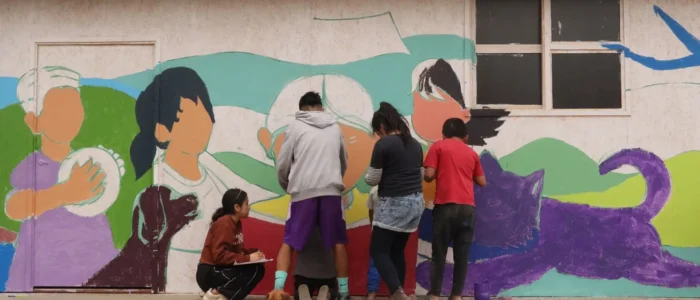 Children and adults painting a vibrant mural as part of a Warmi Huasi community art initiative in Peru.